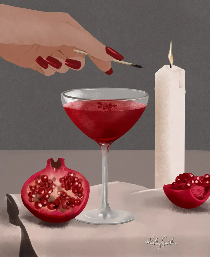 Hand with red nails and cocktail glass with pomegranate and candle