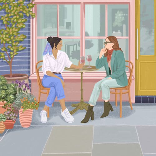 Two women drinking coffee and chatting at outdoor café seating