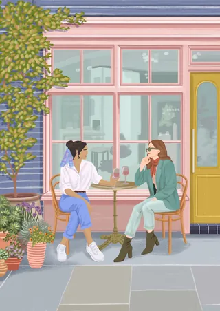 Two women drinking coffee and chatting at outdoor café seating