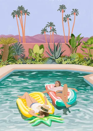Two women lounging on pool floats with tropical plants and palm trees.