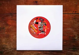 Vinyl record with red label on wooden surface in white sleeve