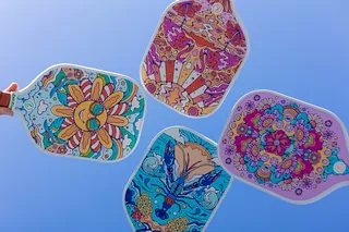 Four vibrant hand fans with intricate colorful patterns held against a clear sky