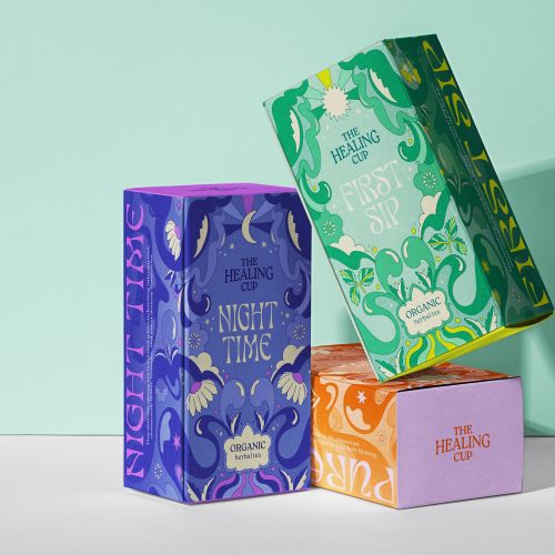 Three colorful The Healing Cup tea boxes in green, purple, orange, and pink