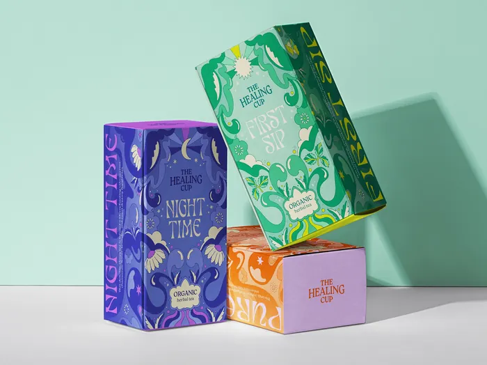 Three colorful The Healing Cup tea boxes in green, purple, orange, and pink