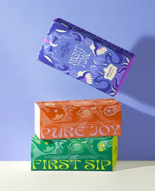 Stack of three vibrant tea boxes with decorative designs on purple surface