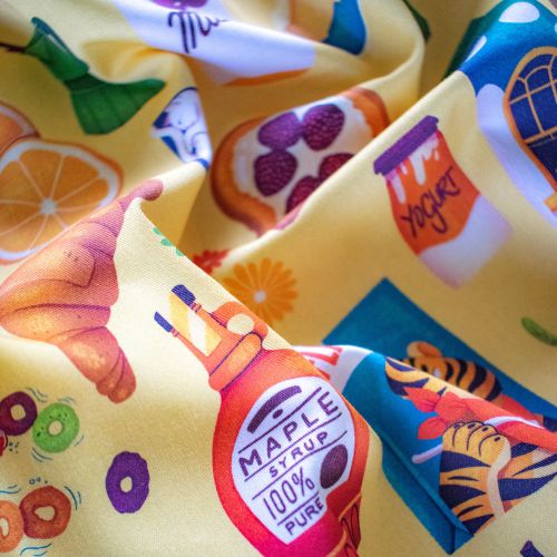 Fabric with illustrations of croissant, maple syrup, honey, and fruits.