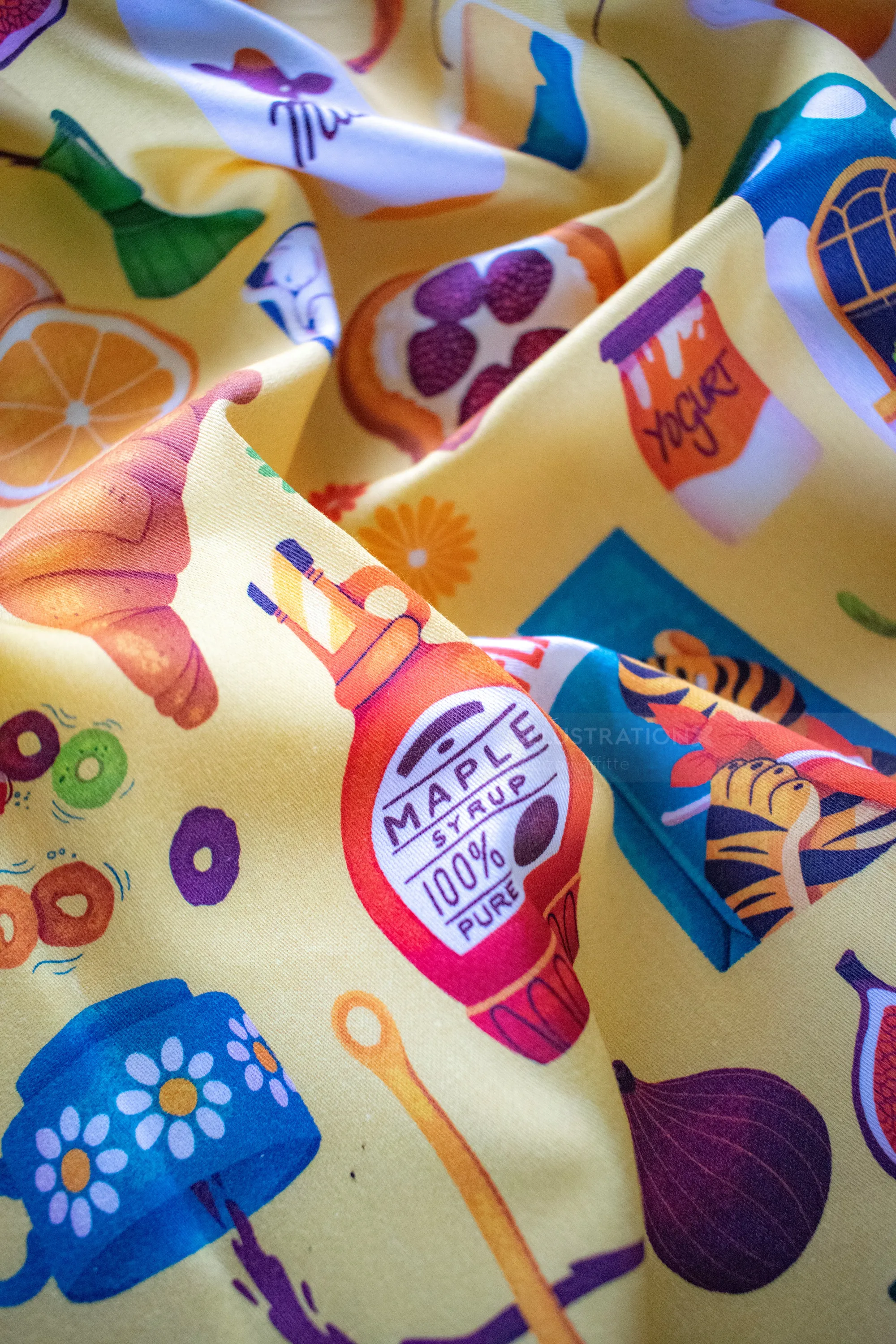 Fabric with illustrations of croissant, maple syrup, honey, and fruits.