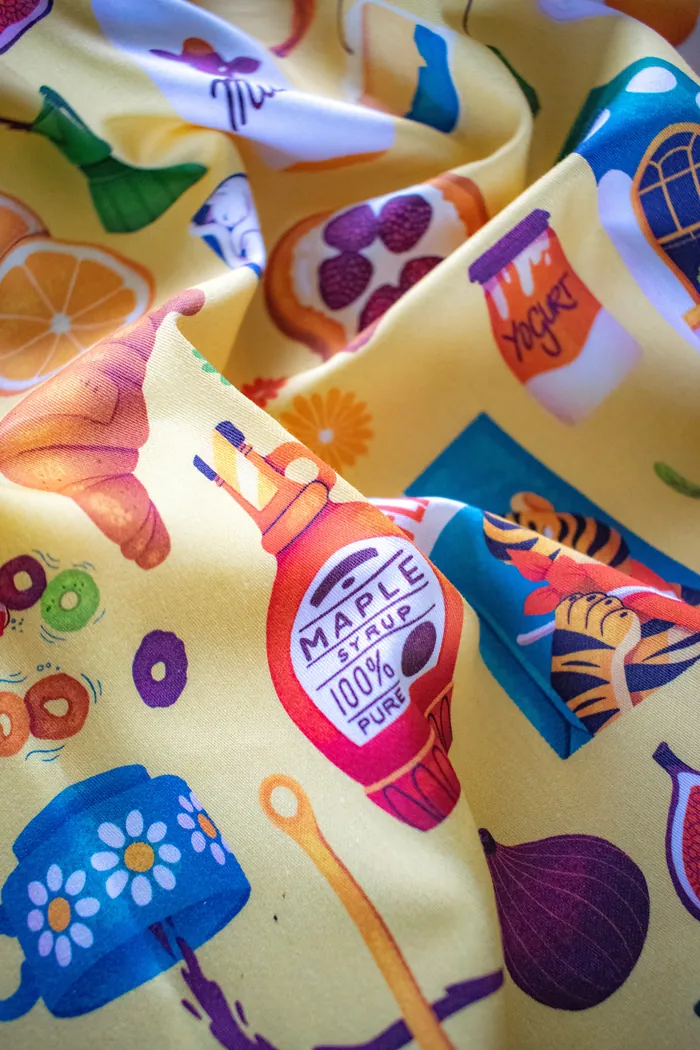 Fabric with illustrations of croissant, maple syrup, honey, and fruits.