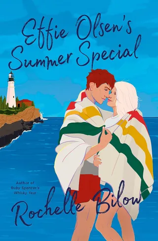 Couple wrapped in striped blanket standing near lighthouse by ocean