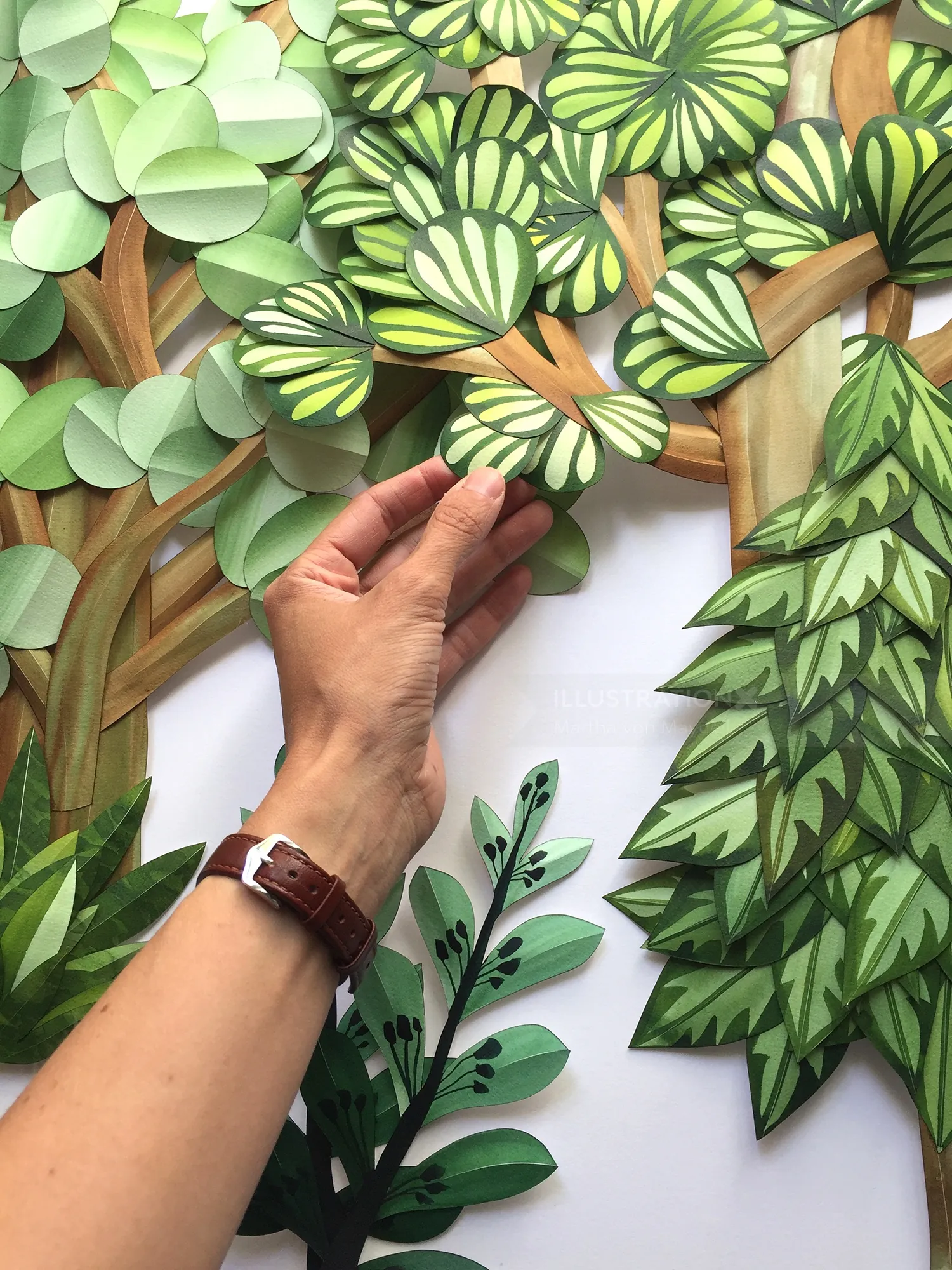 Hand arranging paper cutout leaves in various green patterns by Martha von Maydell