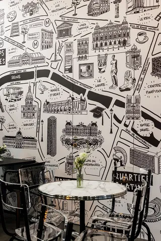 Cafe table with flower vase and black chairs in front of illustrated city map wall