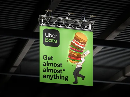 Uber Eats banner showing a person carrying a large burger advertisement by Max Erwin