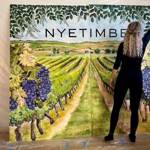 Woman painting a vineyard mural with Nyetimber text and grapevines