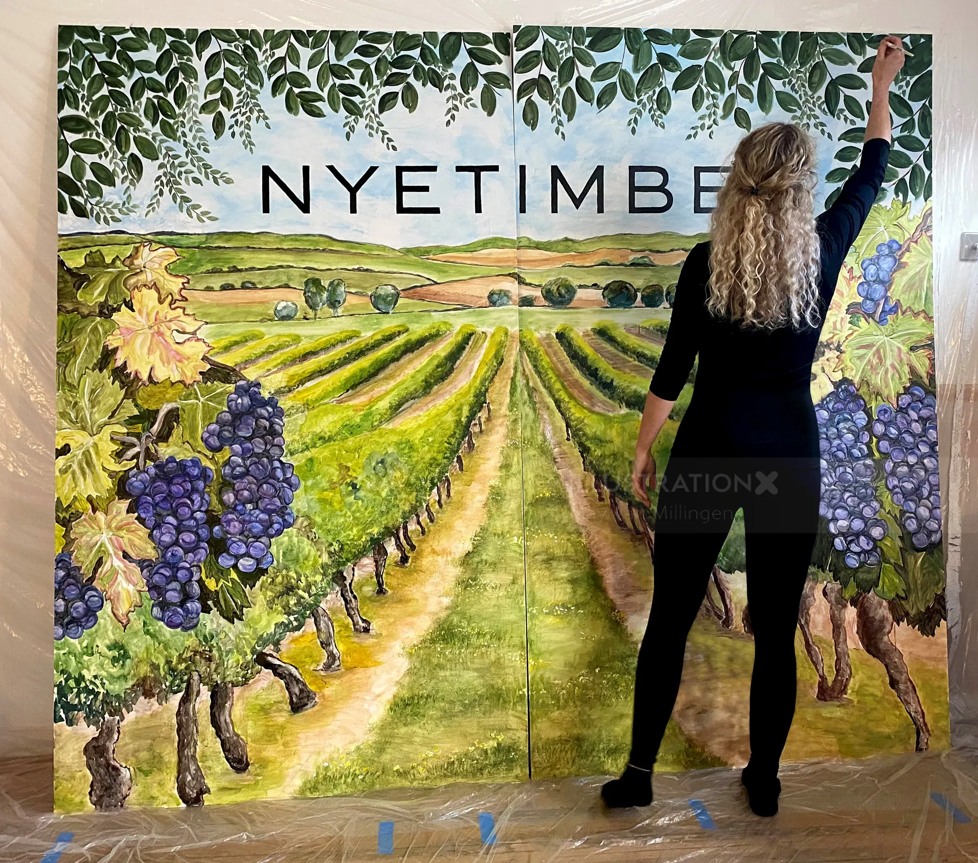 Woman painting a vineyard mural with Nyetimber text and grapevines
