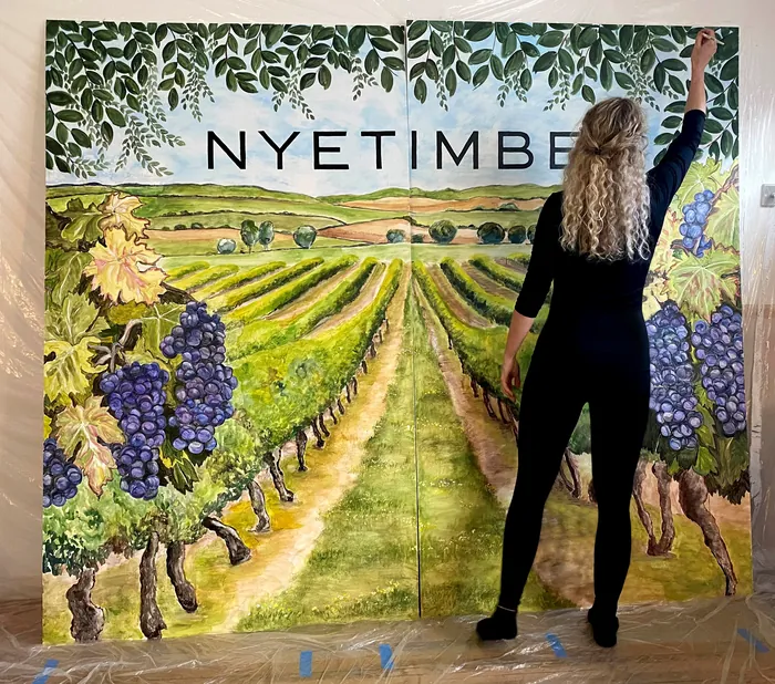 Woman painting a vineyard mural with Nyetimber text and grapevines