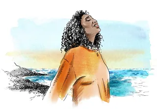 Woman standing by the ocean with eyes closed and smiling