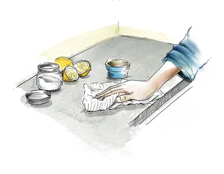 Hand cleaning kitchen sink with cloth and lemon halves nearby