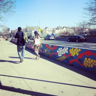 People walking past colorful floral mural on city sidewalk