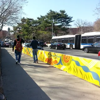 Colorful mural alongside city sidewalk with pedestrians and buses