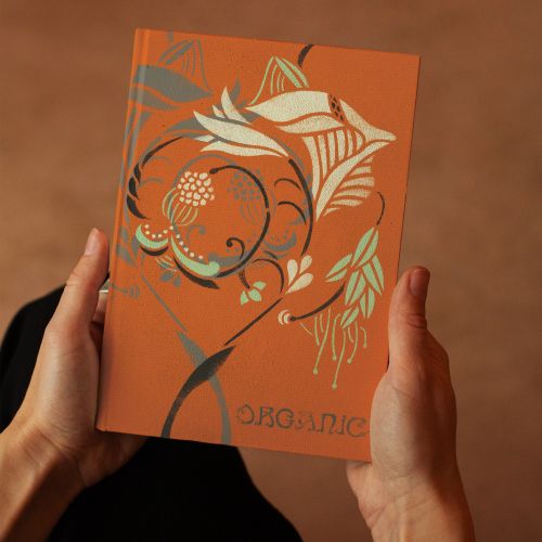 Hands holding an orange book cover with floral stencil art