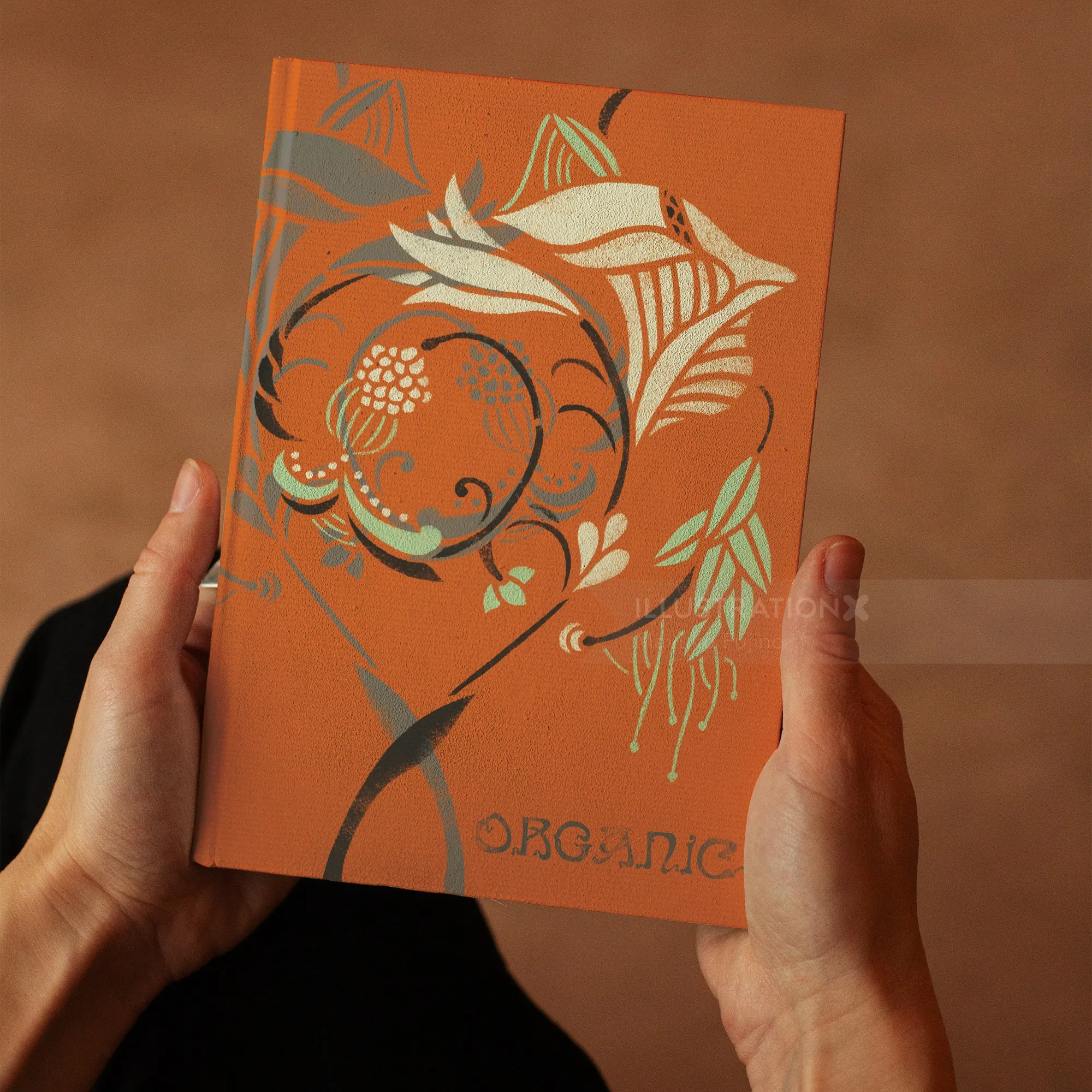 Hands holding an orange book cover with floral stencil art