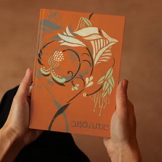 Hands holding an orange book cover with floral stencil art
