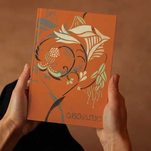 Hands holding an orange book cover with floral stencil art