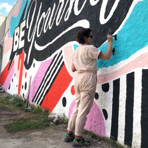 Artist Mel Cerri painting colorful Be Yourself mural on wall