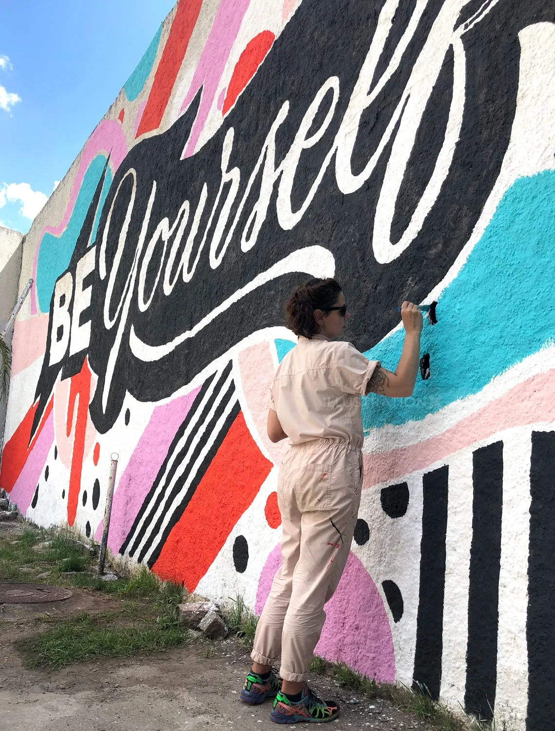 Artist Mel Cerri painting colorful Be Yourself mural on wall