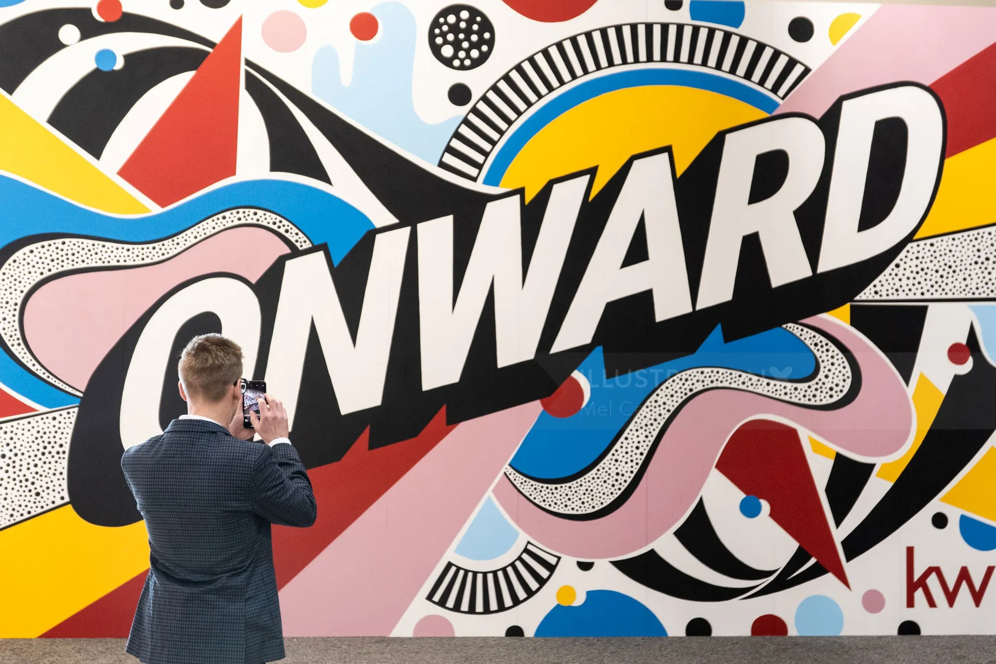Man photographing colorful Onward mural by Mel Cerri