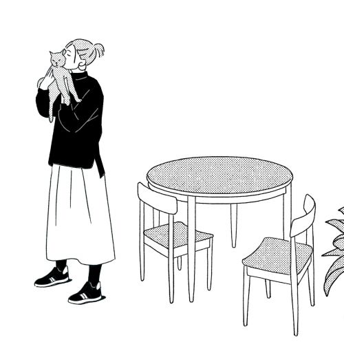 Woman in black sweater holding a cat beside dining table with two chairs