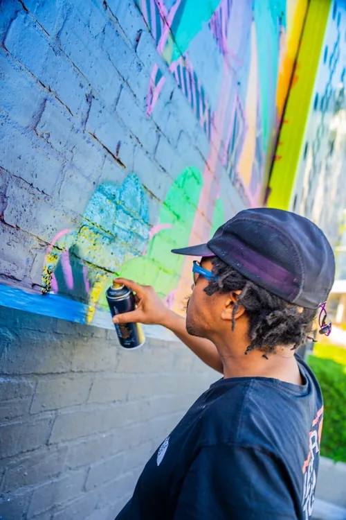 Eine Person sprüht im Freien bunte Graffiti auf eine Backsteinmauer.