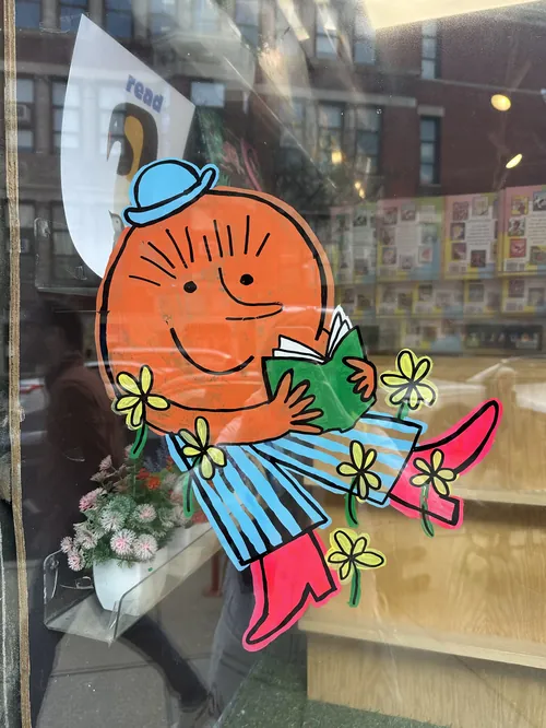 Mural colorido com personagem lendo na vitrine de uma livraria, criado por Ollie Wootton.