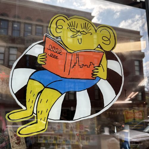 Cartoon character reading book in bookstore window by Ollie Wootton