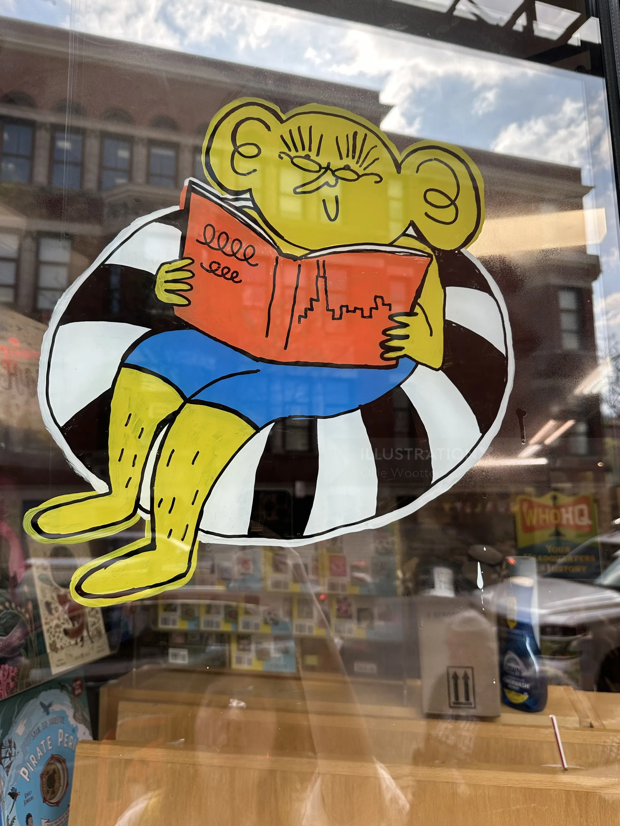 Comicfigur liest Buch im Schaufenster einer Buchhandlung (von Ollie Wootton)