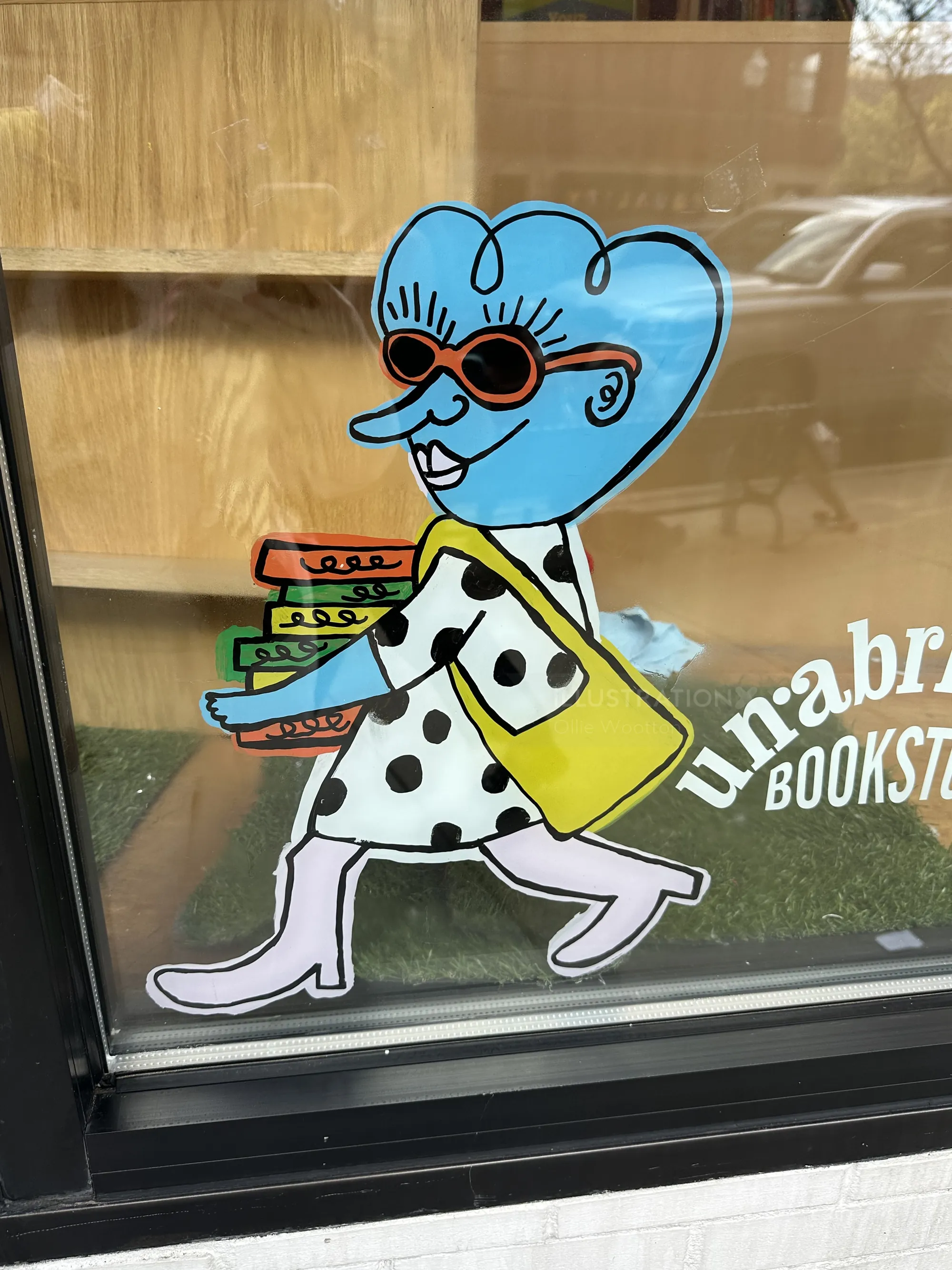 オリー・ウートンによる壁画「Unabridged Books」に登場する、青い髪の漫画風女性が本を運んでいる様子
