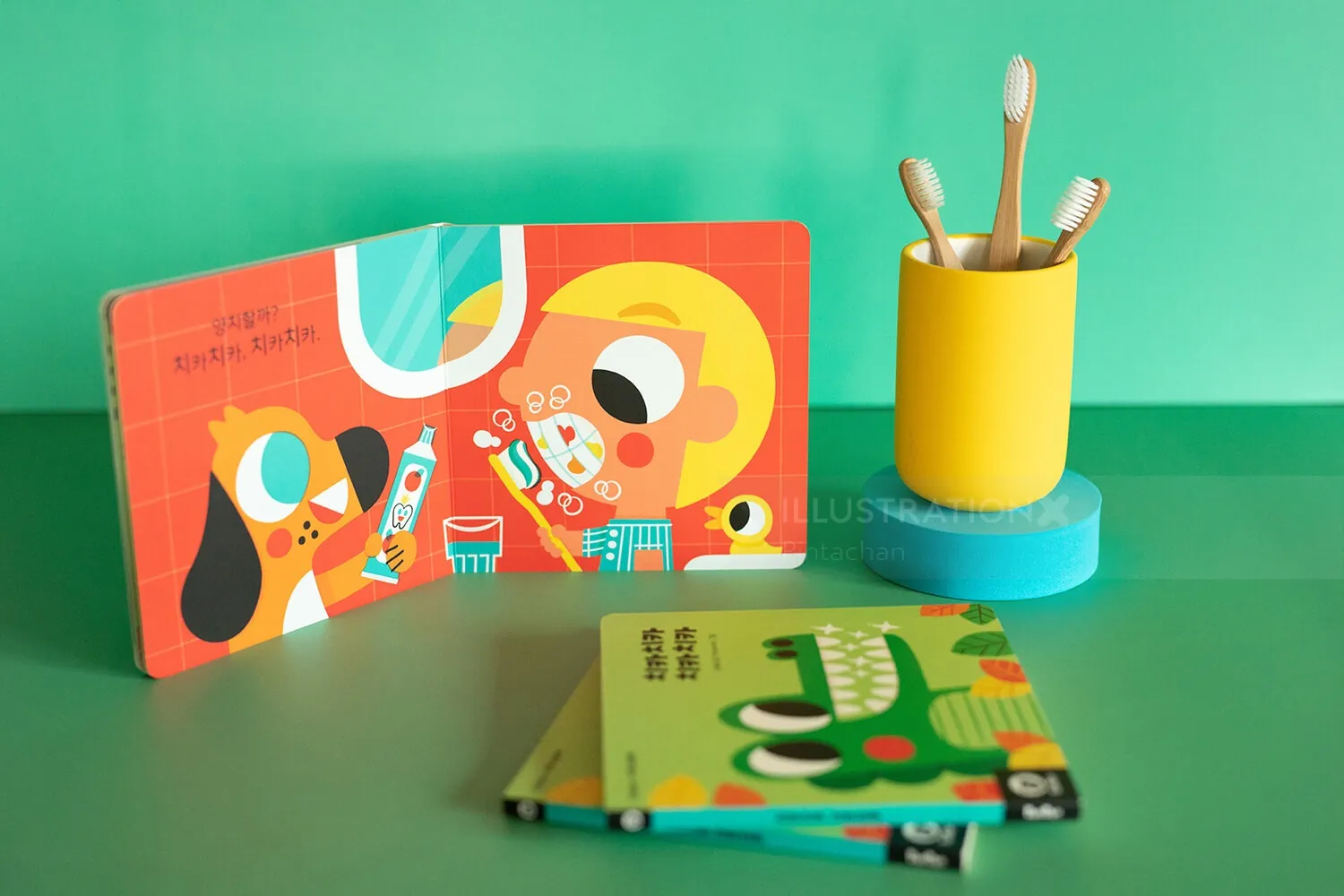 Children's books with colorful illustrations next to a yellow brush holder by Pintachan