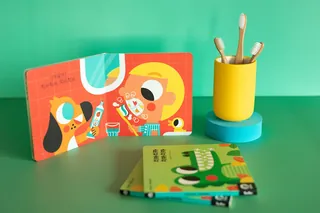 Children's books with colorful illustrations next to a yellow brush holder by Pintachan