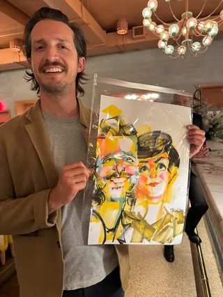 Man smiling while holding a colorful abstract portrait artwork