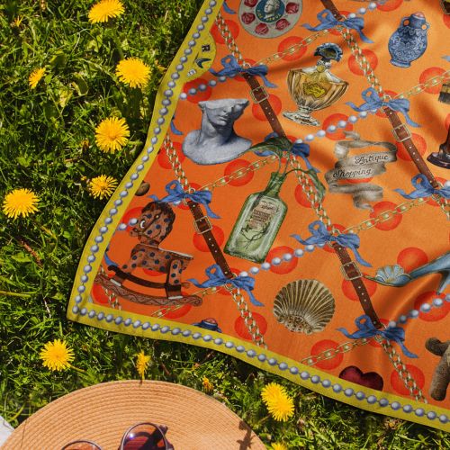 Orange vintage-themed scarf laid on grass surrounded by yellow dandelions.