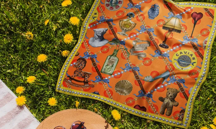 Orange vintage-themed scarf laid on grass surrounded by yellow dandelions.