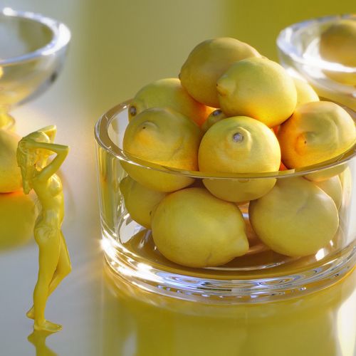 Glass bowls filled with lemons on a yellow reflective surface by RIVE GAUCHE