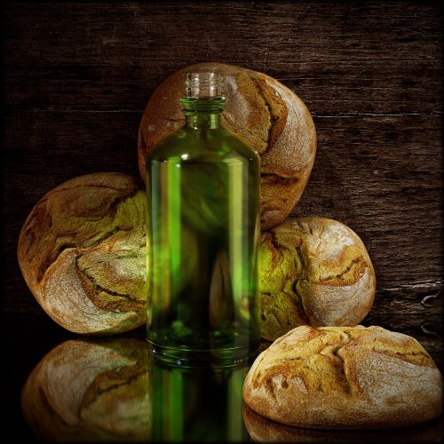 Green glass bottle with rustic bread loaves on wooden background by RIVE GAUCHE