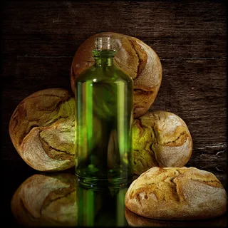 Green glass bottle with rustic bread loaves on wooden background by RIVE GAUCHE