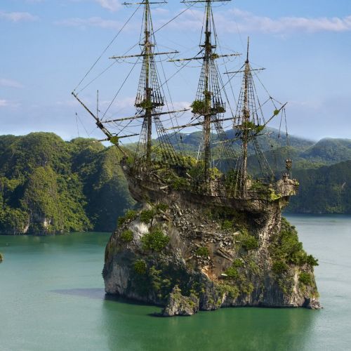 Old sailing shipwreck on rocky island in green water by mountainous coast by RIVE GAUCHE