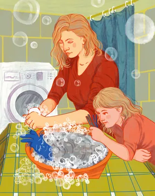 Mother and child hand washing clothes with soap bubbles in laundry room