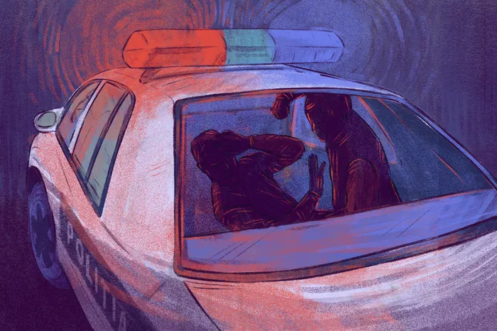 Person seated in rear of police car with flashing lights at night