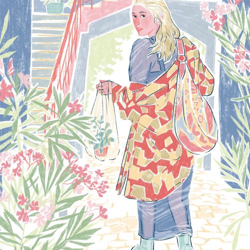 Woman in patterned coat walking among plants and flowers outdoors.