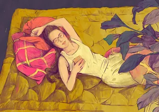 Woman resting on yellow blanket with pink pillows using a smartphone