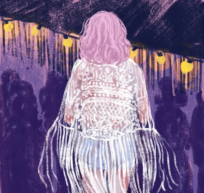 Person with pink hair in fringed outfit standing under yellow hanging lights
